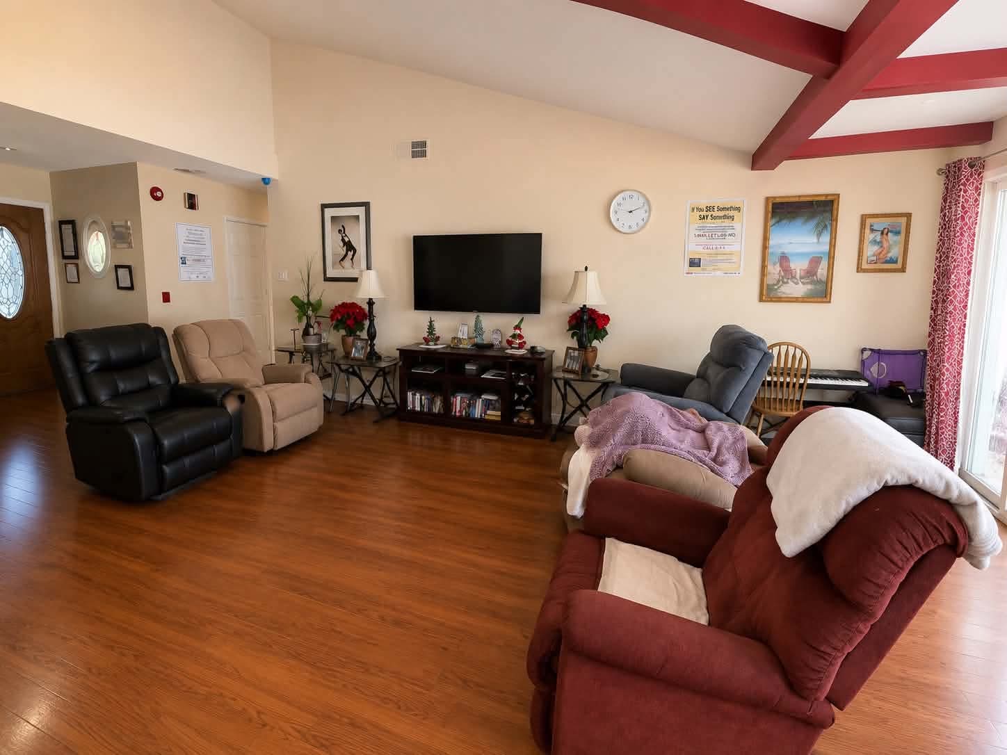 The bright, open shared living room at Tessa Place 2 with comfortable recliners, a wall-mounted TV, and natural light.