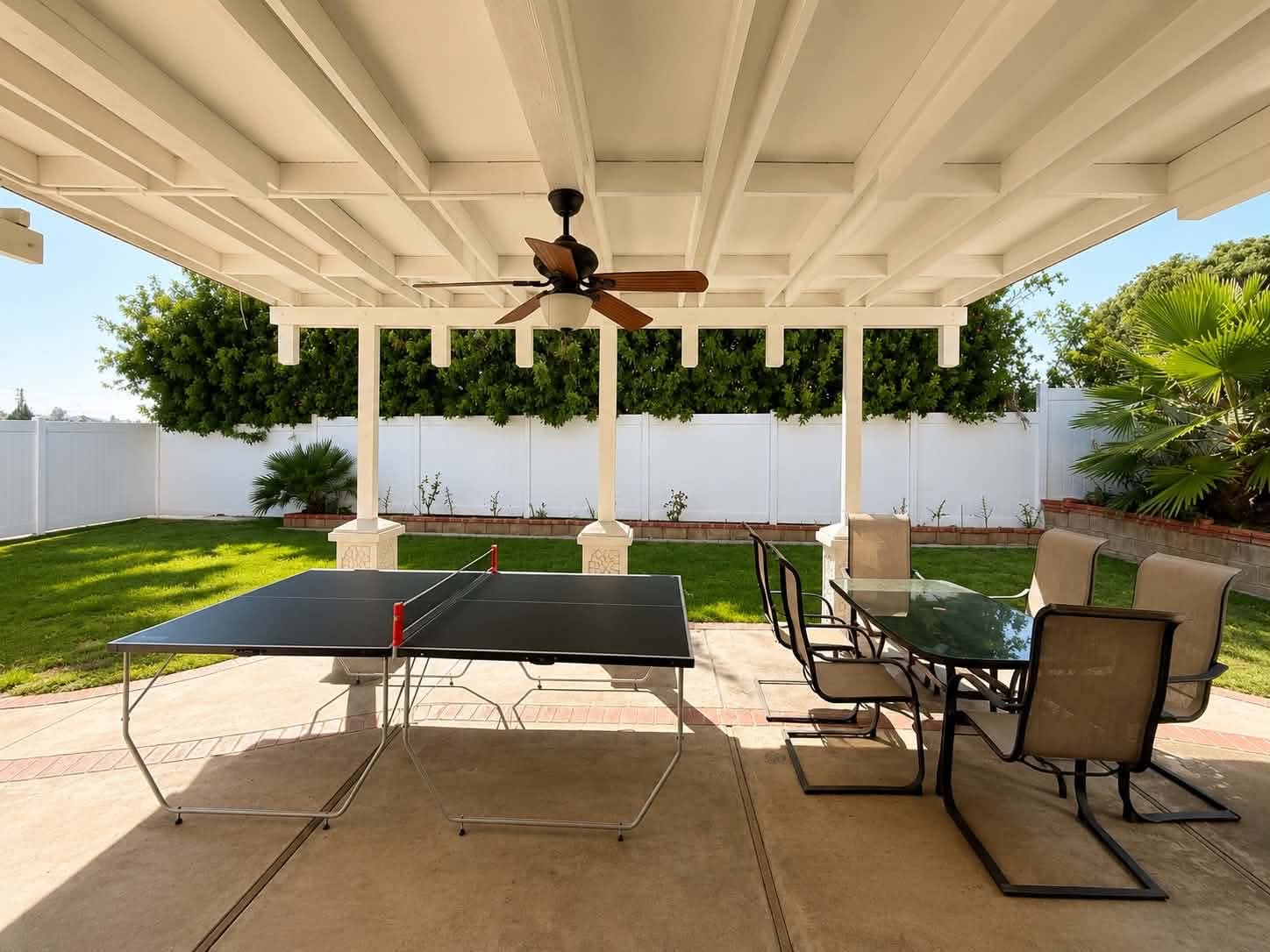 The covered backyard patio at Tessa Place 2 with seating, a ceiling fan, and a green lawn.